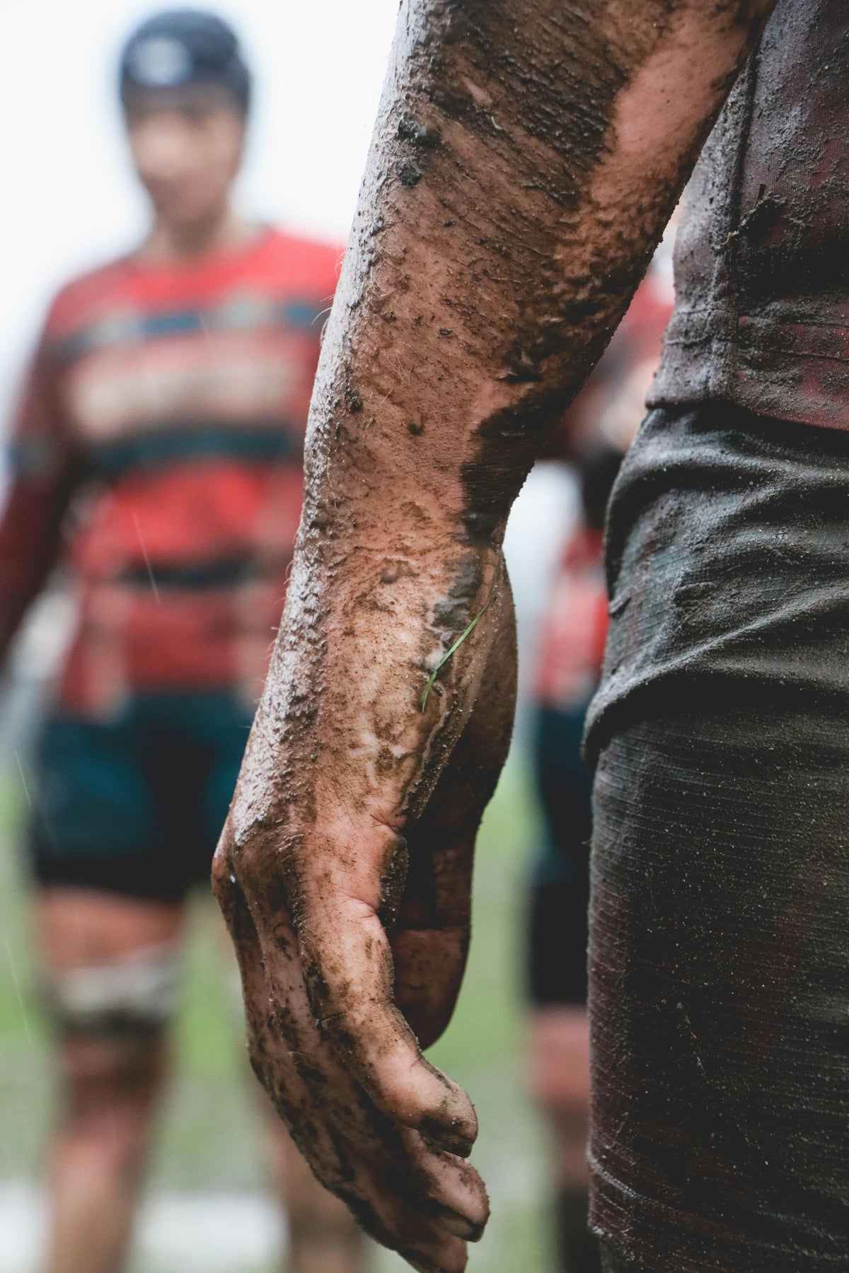 Muddy arm of a rugby player with another player in the background playing For Elk Sports Nutrition